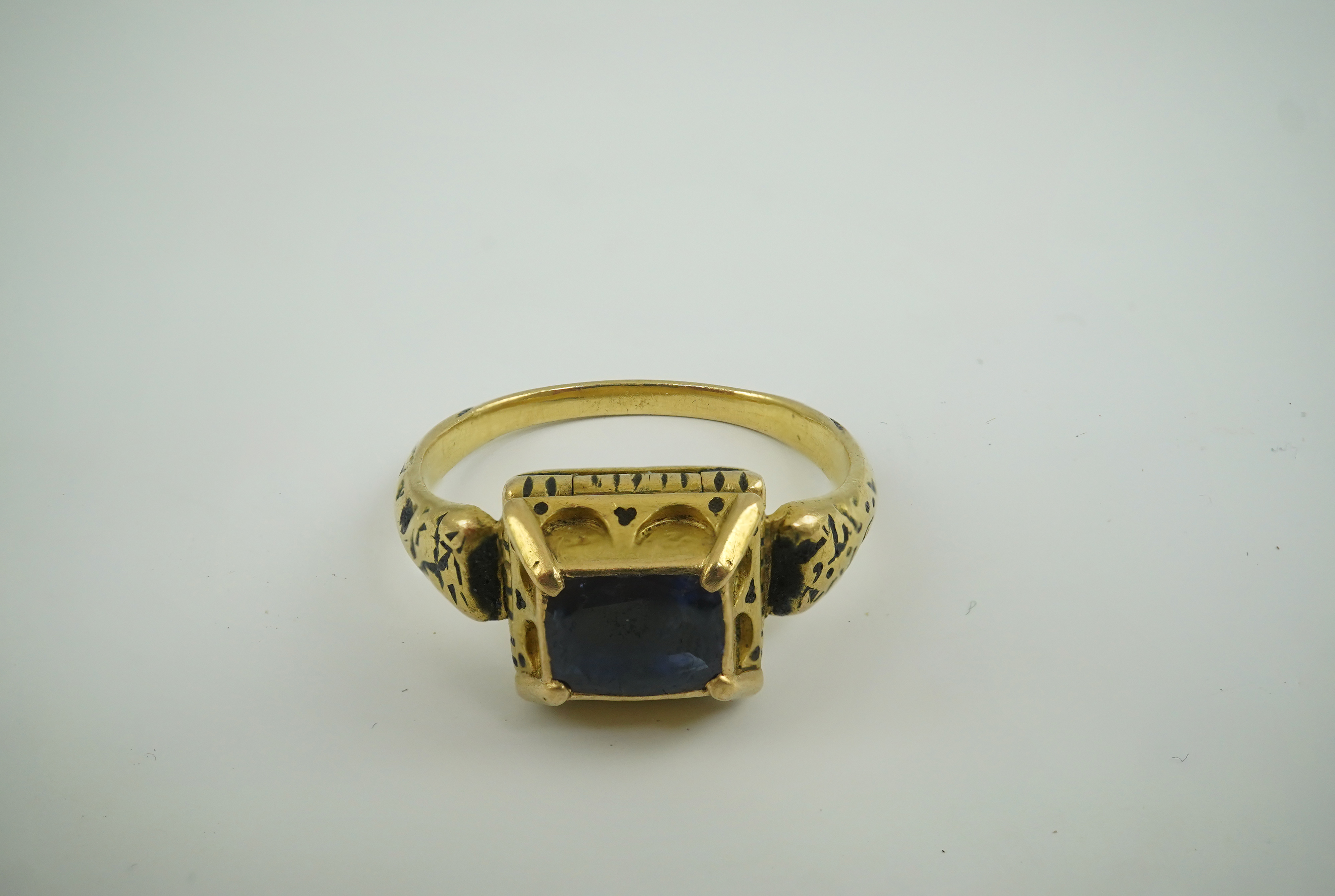 An antique high carat gold, black enamel and later? collet set cushion cut sapphire set 'poison' ring